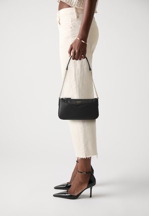 Black leather clutch bag with gold chain strap; features a textured finish and a zip closure. Model wears light-colored cropped jeans and heels.