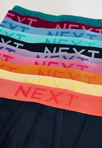 Színes boxeralsók rugalmas pántokkal, amelyeknek kontrasztos hímzett szövegük van: "NEXT". Különböző árnyalatokban elérhetőek, beleértve a sötétkéket, a türkizt, a rózsaszínt, a narancsot és a sárgát.