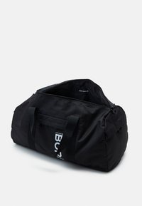 Svart duffelbag laget av slitesterkt stoff, med en stor glidelåsåpning, frontlomme og merkevarenavnet trykket i hvitt.