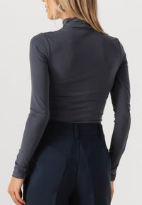 Aansluitende donkergrijze lange mouw top met een hoge halslijn, gecombineerd met marineblauwe high-waisted broek met achterzakken en een vlakke voorkant.