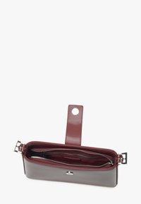 Burgundská kožená peněženka s hladkým povrchem, zipovými přihrádkami, patentním uzávěrem a odnímatelným popruhem pro snadné nošení.