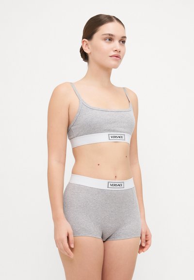 Szürke pamut bralette vékony pántokkal és fehér elasztikus szalaggal, rajta a "VERSACE" logóval. Hozzá illő szürke pamut rövidnadrággal párosítva. Egyszerű dizájn.