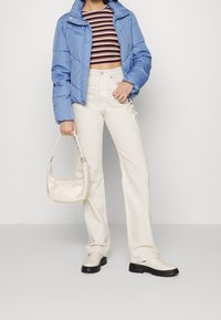 Blauer Puffer-Jacke, verkürzter gestreifter Top, weiße weite Hose, helle Handtasche mit Seilgriff und beige Boots mit dicker Sohle.