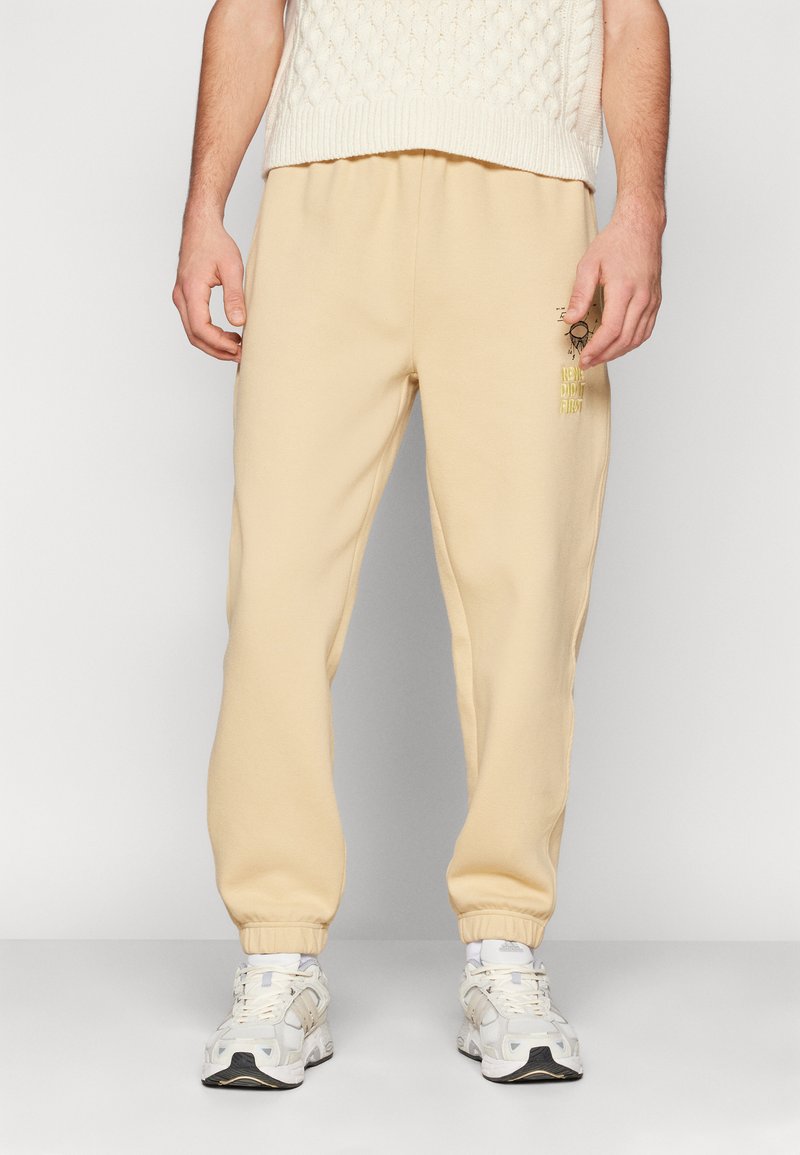 Tan joggingbroek met elastische boorden, voorzien van een gele bedrukking. Gemaakt van zacht materiaal, hebben ze een relaxte pasvorm en een comfortabele tailleband.