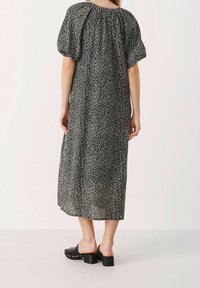 Vestido maxi de estampado en blanco y negro con mangas abullonadas, escote elástico y tela fluida. Combinado con sandalias de tacón negras.