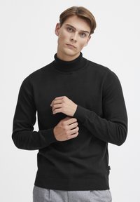 Maglione a collo alto nero realizzato in tessuto a maglia liscia, con polsini e orlo a coste, dalla vestibilità rilassata e design minimalista.