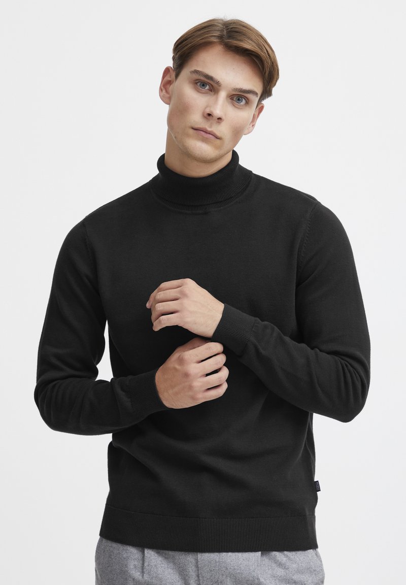 Maglione a collo alto nero realizzato in tessuto a maglia liscia, con polsini e orlo a coste, dalla vestibilità rilassata e design minimalista.