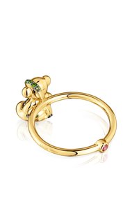 Anello color oro con un design di orso, gemme verdi e un accento rosa, finitura lucida, forma organica e marchio ben visibile.