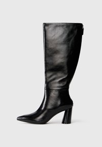 Bota de cuero negro hasta la rodilla con punta afilada, textura suave y un tacón grueso. Presenta un detalle de cremallera en la parte de atrás.