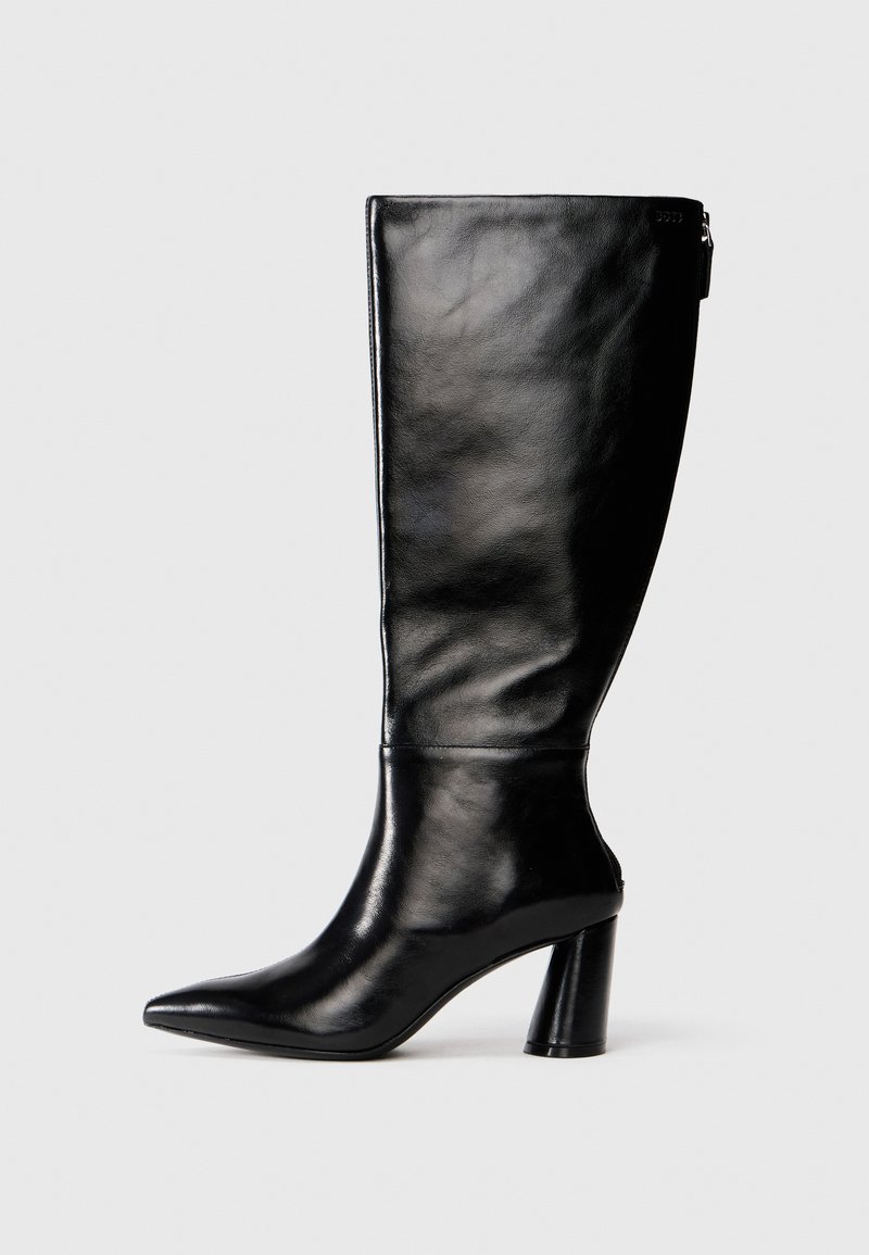 Bota de cuero negro hasta la rodilla con punta afilada, textura suave y un tacón grueso. Presenta un detalle de cremallera en la parte de atrás.
