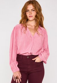 Blusa a righe rosa con maniche lunghe e ampie e scollatura a V, abbinata a pantaloni attillati bordeaux scuro con tasche frontali.