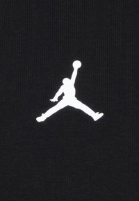 Tessuto nero con un logo Jumpman bianco ben visibile, che rappresenta il profilo di una persona in volo, mentre tiene un pallone da basket.
