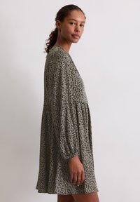 Kwiatowa sukienka w ciemnozielonym kolorze z białymi wzorami, z długimi rękawami i luźnym krojem. Materiał ma miękką, lekką teksturę.