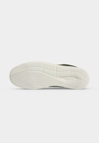 Semelle en caoutchouc blanc d'une basket avec des motifs texturés antidérapants et des indentations rectangulaires, montrée sur un fond clair uni.