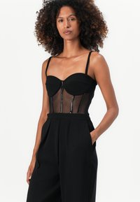 Schwarzer Body mit einem taillierten Oberteil, transparentem Mesh-Mittelteil und dünnen Trägern. Verfügt über ein strukturiertes Design und einen Reißverschluss entlang der Vorderseite.
