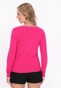 Pulover lung din tricot, ajustat, de culoare roz aprins. Prezintă un decolteu rotund cu o margine albă în contrast și manșete și tiv cu model côté.