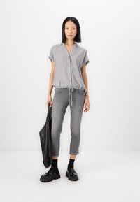 Gestreifte kurzärmelige Bluse in Grau und Weiß, mit Kordelzugsaum, kombiniert mit figurbetonten grauen Jeans und klobigen schwarzen Plateauschuhen. Schwarze Tote-Bag.