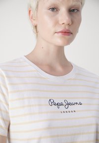 Hvit t-skjorte med gule striper, rund hals og blå "Pepe Jeans London" logo på forsiden. Myk bomullsstoff, kortermet.