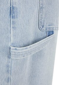 Heled sinine denimpind, millel on eesmine tasku. Tekstuur on kergelt kulunud, nähtava õmblusega ja tasase taskuava vormiga.