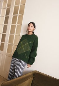 Green fuzzy sweater with a diamond pattern in lighter green, paired with navy and white striped pants. Soft texture, oversized fit.