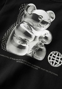 Ours en bonbon argenté réfléchissant avec une ombre en damier déformée à côté d'une icône de globe sur un tissu noir avec un texte motivant en dessous.