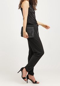 Mono negro sin mangas con un corte relajado, combinado con sandalias de tacón alto negras y un bolso de mano estructurado negro. Textura suave.