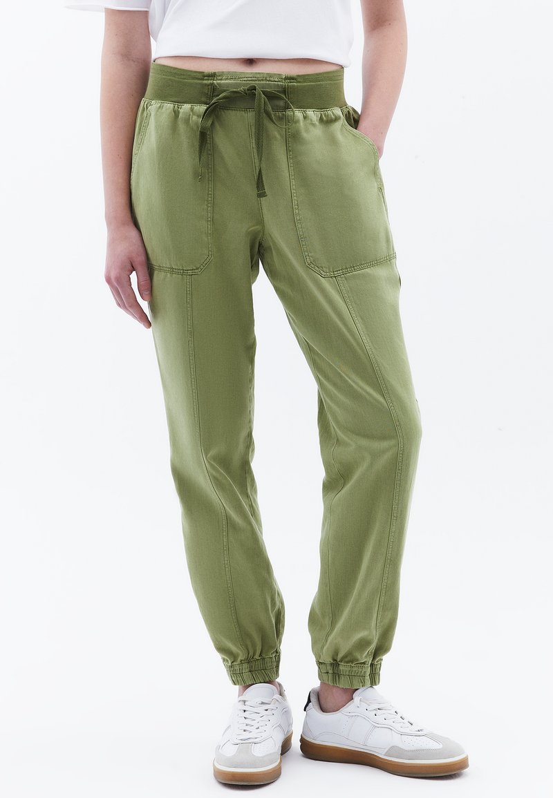 Pantalones de algodón verde claro con cintura elástica, cordón, bolsillos laterales y piernas ajustadas, combinados con zapatillas blancas.