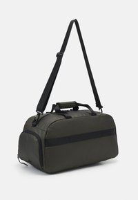 Saco tipo duffel verde-escuro, feito de material resistente, com uma alça preta e elementos de contraste, fecho com zíper e faixa de contraste.