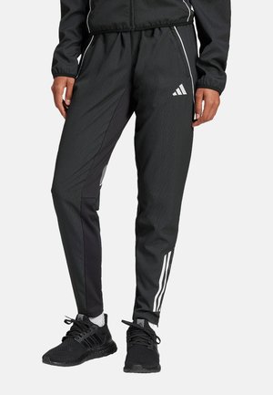 Pantalons de sport noirs avec une coupe fuselée, présentant des panneaux latéraux noirs contrastants et des rayures blanches Adidas le long des jambes.
