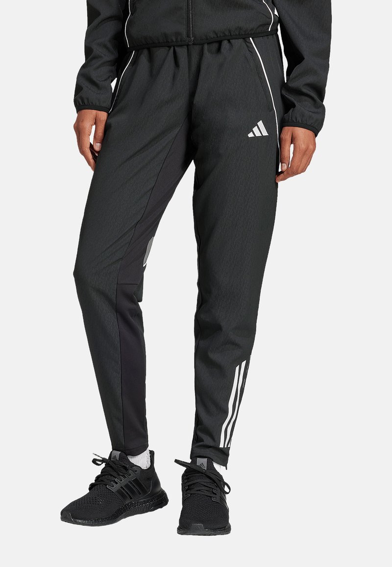 Pantalons de sport noirs avec une coupe fuselée, présentant des panneaux latéraux noirs contrastants et des rayures blanches Adidas le long des jambes.