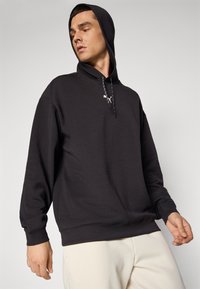 Sudadera negra con cordón, de corte holgado, hecha de material suave, con un logo en el pecho y puños y dobladillo acanalados.