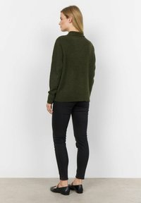 Skogsgrön stickad tröja med hög krage, avslappnad passform och långa ärmar, tillsammans med svarta slim fit-jeans och svarta platta skor.