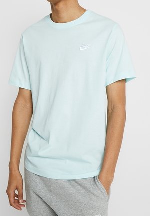 T-shirt en coton bleu clair à manches courtes, col rond, avec le logo blanc de Nike sur la poitrine. Associé à un short gris.