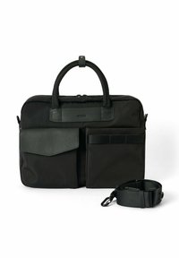 Sort nylon taske med to håndtag, en struktureret læderfrontlomme, to sidelommer og en aftagelig strop. Lynlåslukning ovenpå.