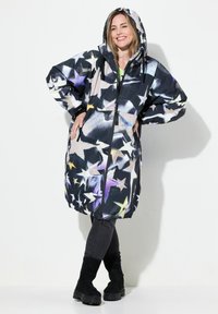 Lång, överdimensionerad svart kappa med stjärnmönster i vitt, gult och lila. Har en huva, framdragkedja och elastiska ärmar. Mjuk material.