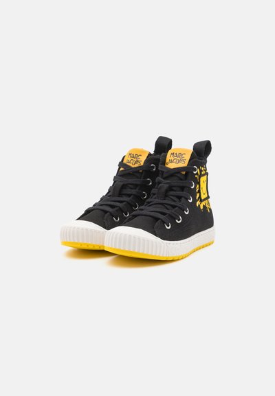 Sneaker alte nere con tomaia in tessuto texturizzato, punta in gomma bianca, suola gialla e dettagli gialli brillanti che presentano un design con faccina sorridente.