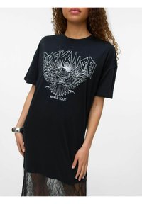 Nainen, jolla on yllään musta ylisuuri T-paitamekko, jossa on teksti "Rock Angel World Tour" ja kotka-graafika, yhdessä pitsihameen ja hopeaketjun kanssa.