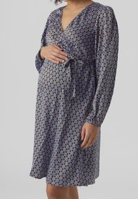 Gravidklänning med V-ringning, långa ärmar, knytdetalj vid midjan och geometriskt mönster i blått, brunt och krämfärgat på ett satinliknande tyg.