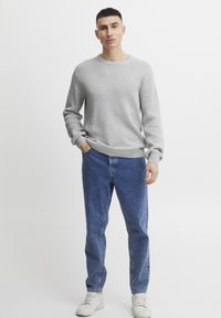 Pulover gri texturat cu guler rotund, combinat cu blugi denim albaștri. Adidași albi completează ținuta, evidențiind un look casual.