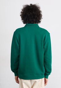 Grønn gensere med krage og ribbestrikkede mansjetter, laget av et mykt, teksturert stoff, med en avslappet passform.