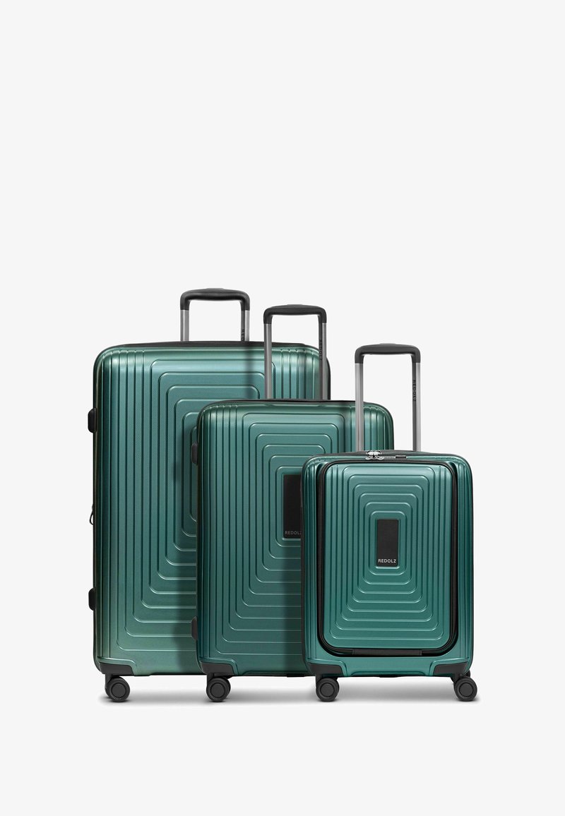 Tre valigie rigide impilate di colore verde scuro, caratterizzate da un design a scanalature lineari, accenti neri, maniglie telescopiche e quattro ruote girevoli.