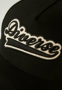 Czarna czapka bejsbolowa z teksturowanej tkaniny, z wyraźnym haftowanym logo "Diverse" w białym kolorze z przodu.