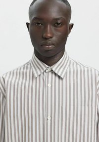 Stripete skjorte med knapper i lys beige og hvit, med standard krage og brystlomme. Jevn stoff med vertikale striper.