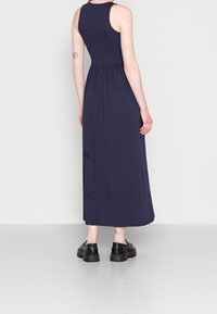 Robe maxi sans manches bleu marine avec un corsage ajusté et une taille froncée, fabriquée en jersey doux. Comprend un ourlet droit et une texture subtile.