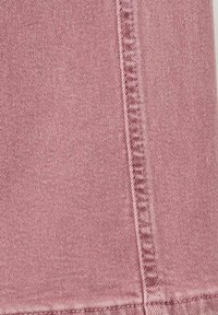 Tela de mezclilla rosa claro con un tejido de sarga diagonal, una costura prominente que corre verticalmente y sutiles variaciones de textura en toda su superficie.