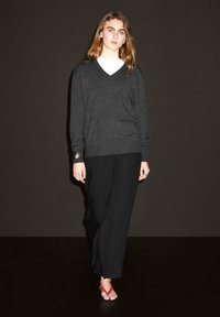 Maglione v-neck grigio scuro, pantaloni neri larghi e infradito rossi. Tessuto morbido, vestibilità rilassata e design minimalista.