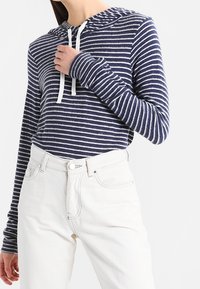 Marineblå och vit randig hoodie i mjukt tyg med dragsko, i kombination med högmidjade vita jeans. Långa ärmar med tumhål.