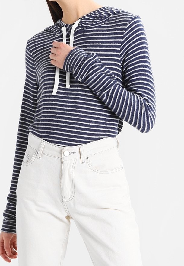 Marineblå och vit randig hoodie i mjukt tyg med dragsko, i kombination med högmidjade vita jeans. Långa ärmar med tumhål.