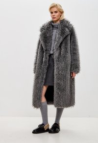 Grå faux pelsovertræk med en bred krave, sideslidser og lange ærmer. Båret over en grå sweater, en nederdel med nålestriber og grå knælange strømper.