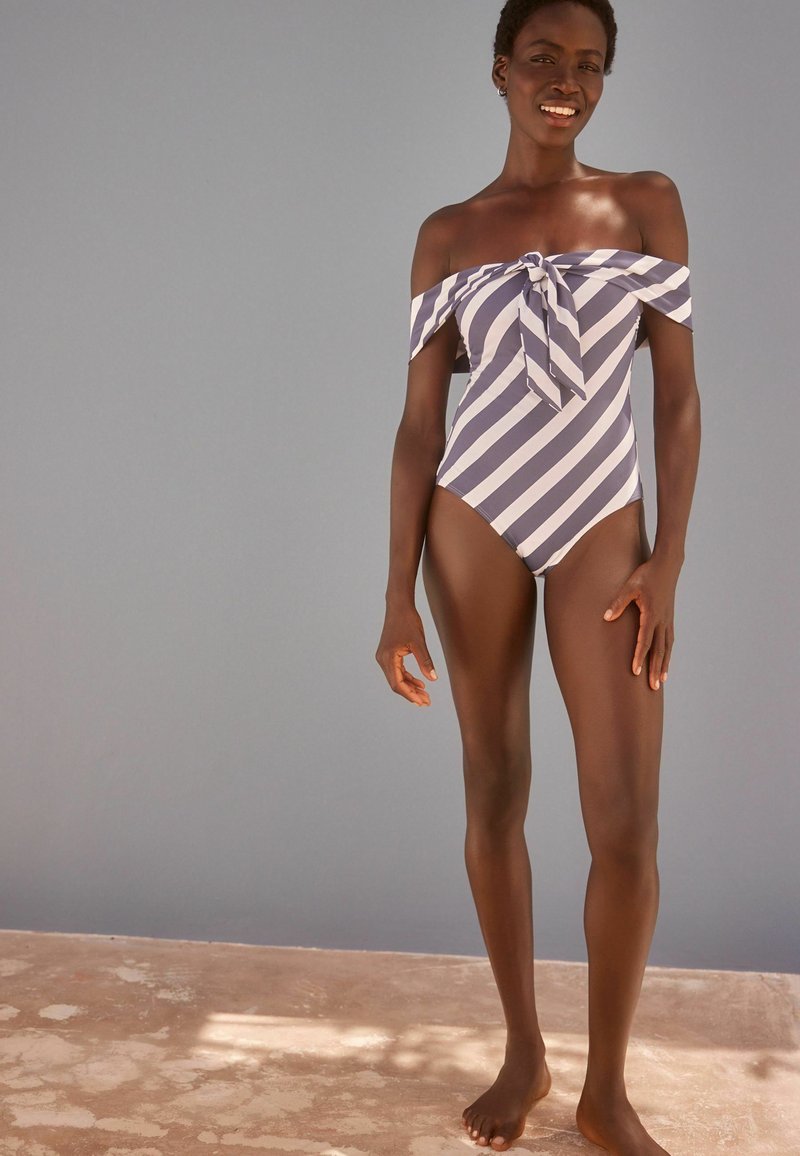 Maillot de bain à épaules dénudées rayé en bleu marine et bleu clair, avec un détail de nœud à l'avant et un tissu lisse, au design ajusté.